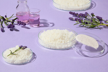 Advertising photo with lavender flowers, essential oils, and bath salts arranged in glass containers on a pastel purple background, ideal for spa treatment promotions.