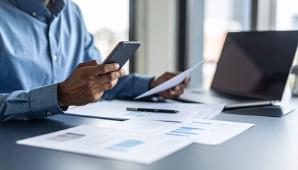 A person flipping through documents on a desk and checking their smartphone