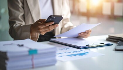 A person flipping through documents on a desk and checking their smartphone