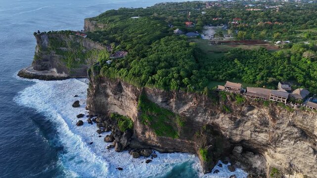Aerial drone footage gliding over Pura Luhur Uluwatu and dramatic cliffs, lush green hills, and ocean shore. Bali, Indonesia	