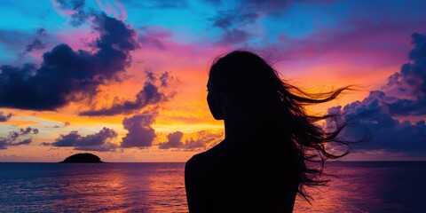 Woman in silhouette with hair blowing in wind, watching island hover among colorful sunset clouds