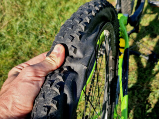 Tire cut by sharp object while riding a mountain bike. Repair by gluing directly on the terrain during a race. Man shows the hole where the puncture occurred