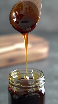 Pouring Viscous Dark Brown Substance From Wooden Spoon Into Glass Jar: Close-Up Stock Video Footage of Thick Molasses or Honey-Like Liquid. Ideal for Food and Cooking Content, Ads, and Recipe