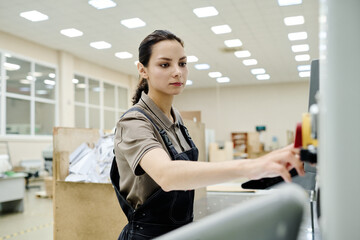 Obraz premium Medium portrait of young woman wearing apron working in print shop operating offset printing press