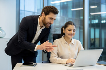 Two colleagues communicate and work together on a laptop in a modern office setting, fostering teamwork, productivity, and a positive working atmosphere, with a professional and corporate environment