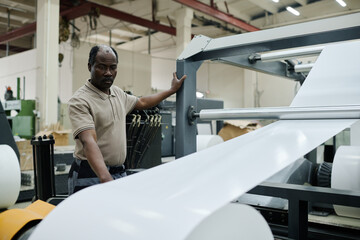 Senior African American man working modern print shop operating flexographic printing press