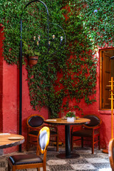 Romantischer Innenhof eines Cafés in Arequipa, Peru. Rote Mauer mit Efeu bewachsen, Holztische und...