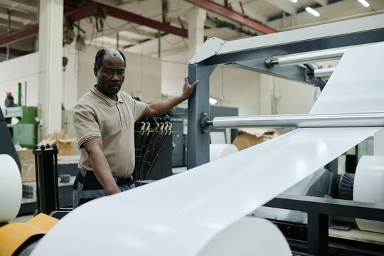 Senior African American man working modern print shop operating flexographic printing press