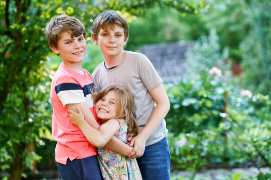 Portrait of three siblings children. Two kids brothers boys and little cute toddler sister girl having fun together in domestic garden. Happy healthy family playing, walking, active leisure on nature