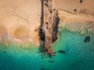 Aerial drone shot of the Santa Maria pier and beach, Sal Island, Cape Verde, at golden sunset. Turquoise waters, fishing boats and a tropical atmosphere in high resolution.
