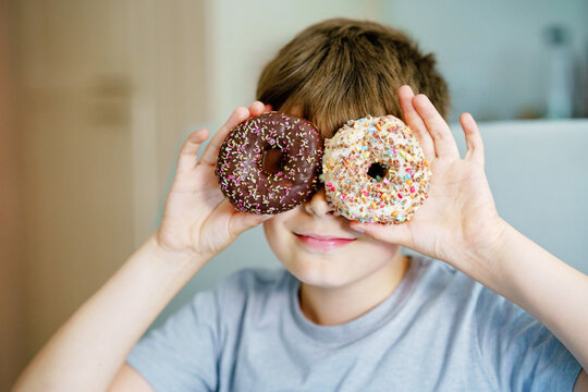 Happy preteen school boy eating sweet donut indoor. Blond child in domestic kitchen or in school canteen Cute kid and unhealthy sugared food.