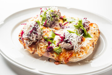 Open-faced sandwich with melted cheese, shredded cabbage, creamy and green sauces on toasted bread, served on a white plate