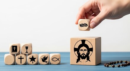 Hand holding a wooden cube with a crown of thorns symbol. Other blocks display Christian symbols and Jesus. Religious concept.