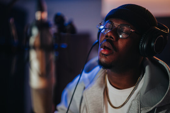 Fototapeta A man wearing headphones and a beanie focuses intently while singing into a microphone during a studio session. The scene conveys deep concentration and passion for music creation.