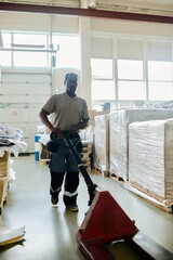 Vertical long shot of mature Black man working in print shop storehouse pulling pallet jack