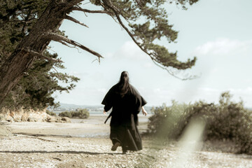 A samurai in black kimono is walking through forest.