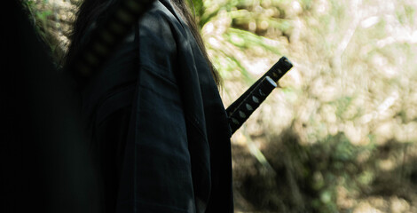 A samurai in black kimono is walking through forest.