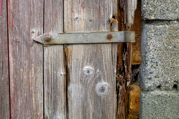Close view of an aged wooden door with a rusty metal latch, displaying decay and peeling paint in...