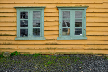 Two turquoise-framed windows adorn a weathered yellow wall, showcasing the rustic beauty of an old...