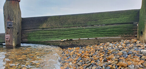 Close-Up of Weathered Wooden Groyne with Algae and Pebbles at Low Tide