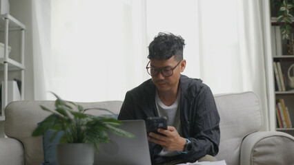 Asian man paying bills online with smartphone at home.