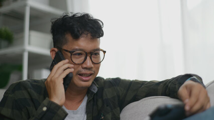 Asian man multitasking by talking on his phone while working on a tablet.