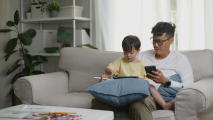Asian father assisting his young son in drawing on a tablet.