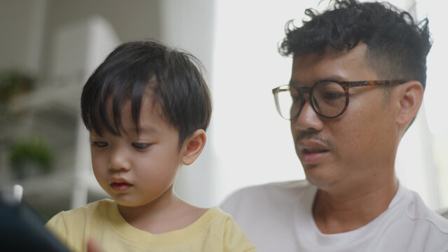 Asian father assisting his young son in drawing on a tablet.