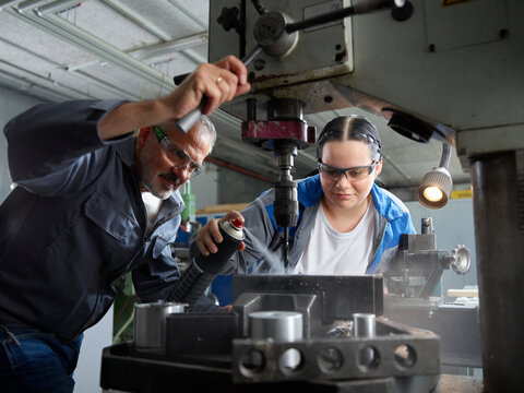 Apprentice spraying lubricant on drill bit by instructor in workshop