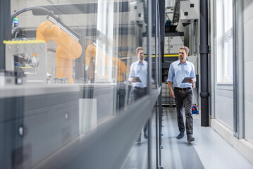 Businessman checking robots with digital tablet in high tech company