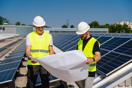 Two technicians discussing plan on the roof of a company building with solar panels