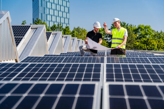 Two technicians discussing plan on the roof of a company building with solar panels