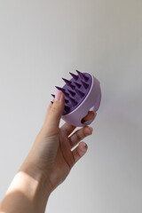 Silicone scalp massage brush in woman’s hand on plain background
