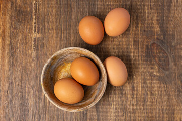 Brown chicken eggs inside a wooden bowl and on a wooden table, viewed from above.