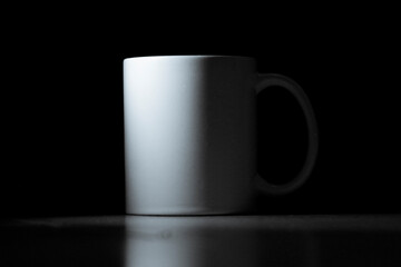 A striking, minimalist studio shot of a simple white ceramic mug, elegantly isolated against a deep black background.