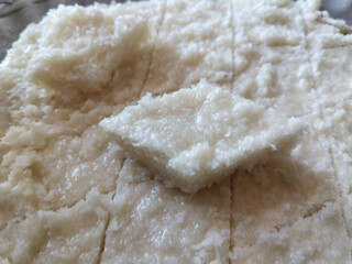 Closeup of traditional Indian coconut halwa made with grated nariyal, evenly spread and textured with knife marks, with a visible square slice placed on top of the sweet
