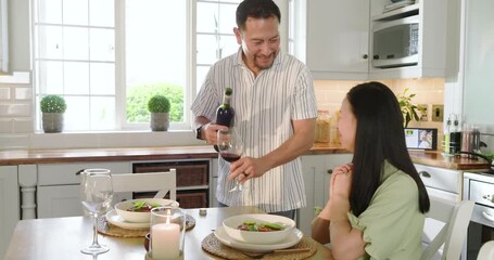 Celebrating anniversary together, Asian couple pouring red wine into glasses at home kitchen - Powered by Adobe