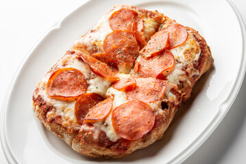 Rectangular pepperoni pizza with thick crust, melted cheese, and herbs on a white plate. Baked to golden perfection, artisanal style, top view.