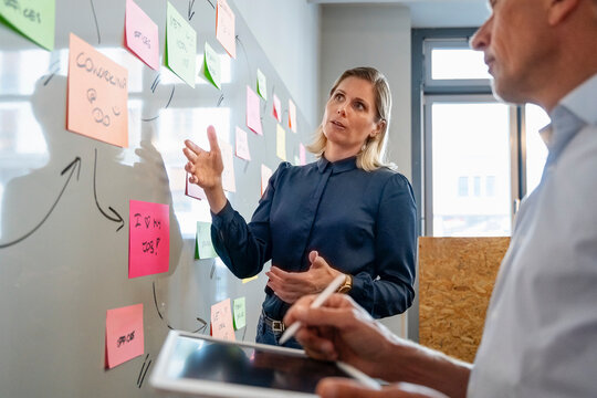 Businesswoman discussing over adhesive notes with colleague holding tablet PC