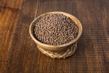 Wooden bowl filled with brown lentils placed on a wooden table, viewed from above.