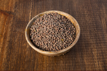 Wooden bowl filled with brown lentils placed on a wooden table, viewed from above.