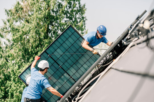 Engineers installing solar panels on roof near tree