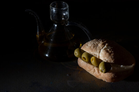 bocadillo de olivas verdes rellenas de anchoas al lado de una aceitera de cristal con fondo oscuro
