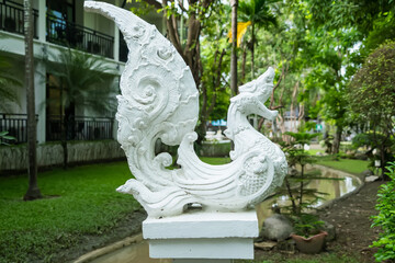 Obraz premium Ornate white stone sculpture of mythical bird with foliage backdrop in a lush garden setting