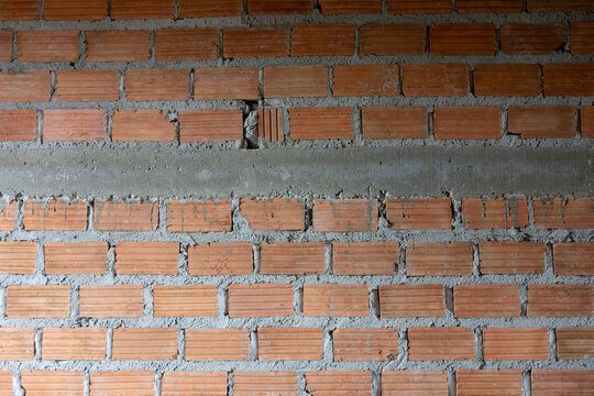Fototapeta A partially constructed red brick wall with visible grey mortar and steel reinforcing bars (rebar), indicating