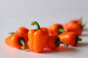 Mini bell peppers presented in a scattered arrangement, featuring vibrant orange pods with green stems