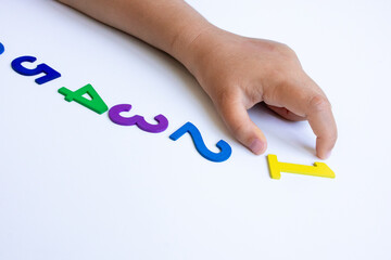 Child hand arranging colorful numbers in sequence on white background
