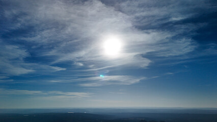 Fototapeta premium Bright sun in the blue sky with wispy clouds and distant horizon