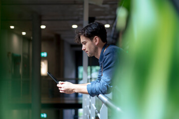Businessman using tablet computer leaning on railing in corridor