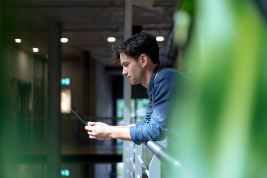 Businessman using tablet computer leaning on railing in corridor
